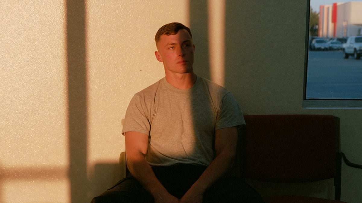 A uniformed soldier waits for a blood draw in a plain military exam room.